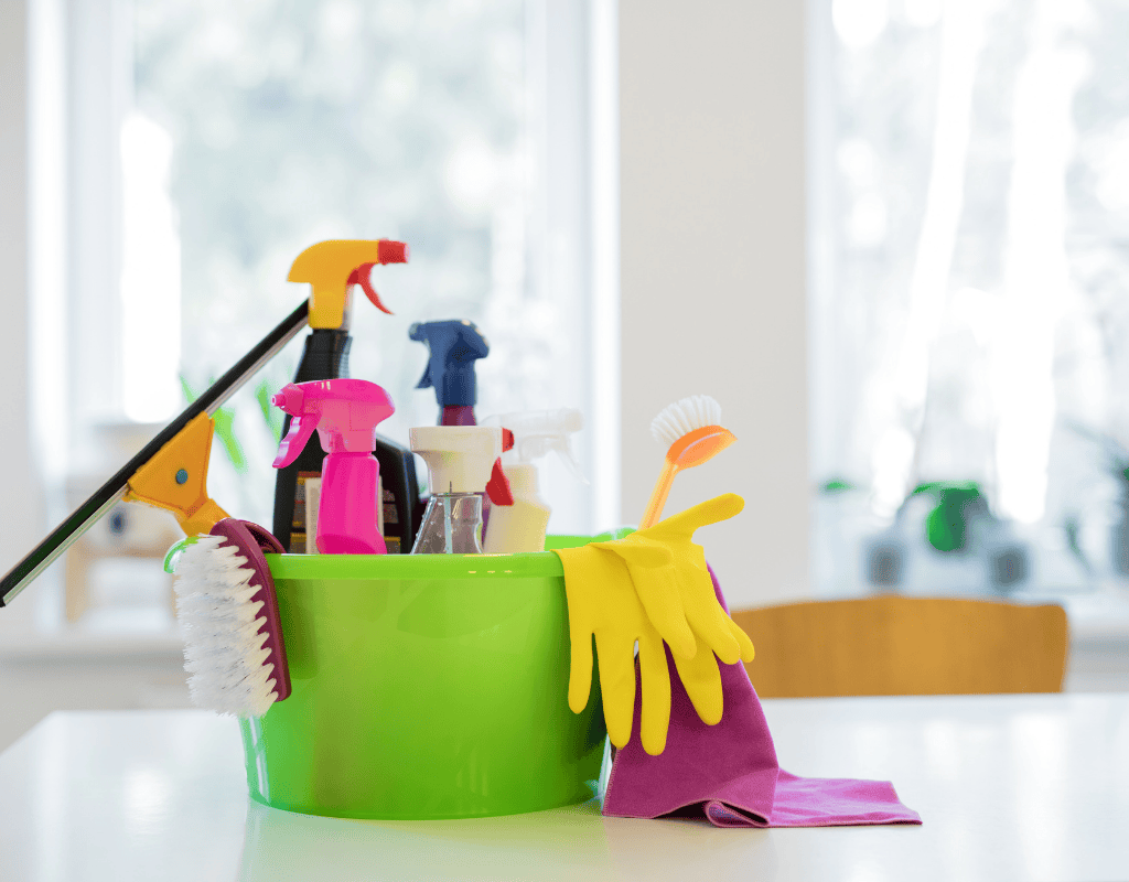 bucket with cleaning supplies including sprays gloves and brushes on table